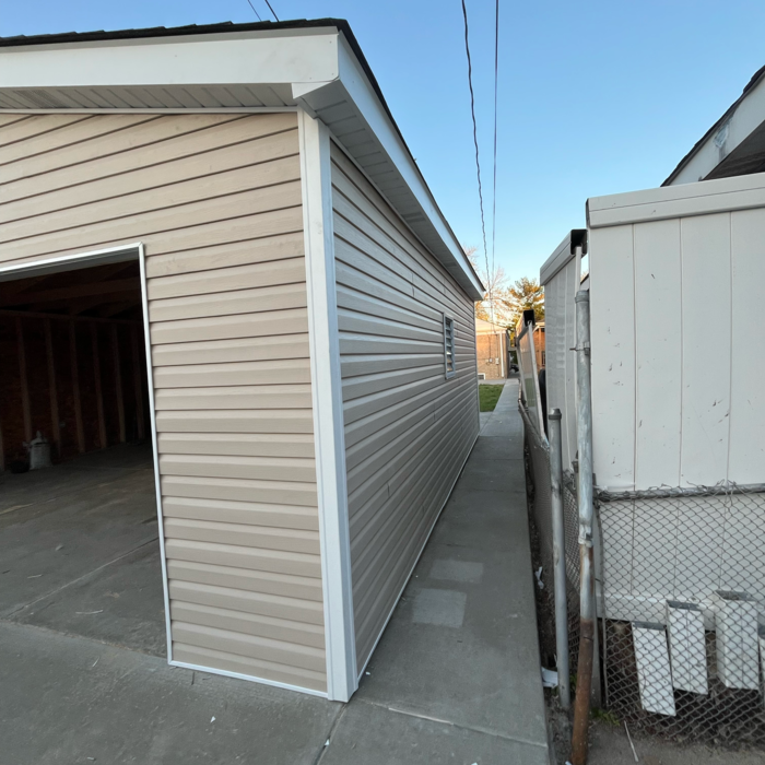 Tan vinyl-sided garage next to a narrow walkway and a chain-link fence.