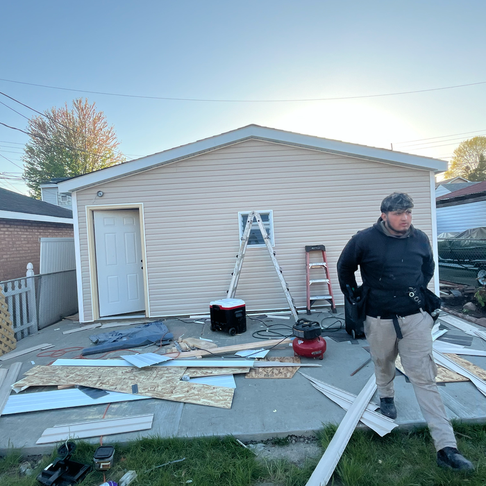 Man walking near a partially sided building with tools and materials strewn about. Construction setting outdoors.