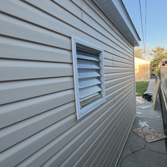 Tan vinyl siding on a building with a white-framed louvered window.