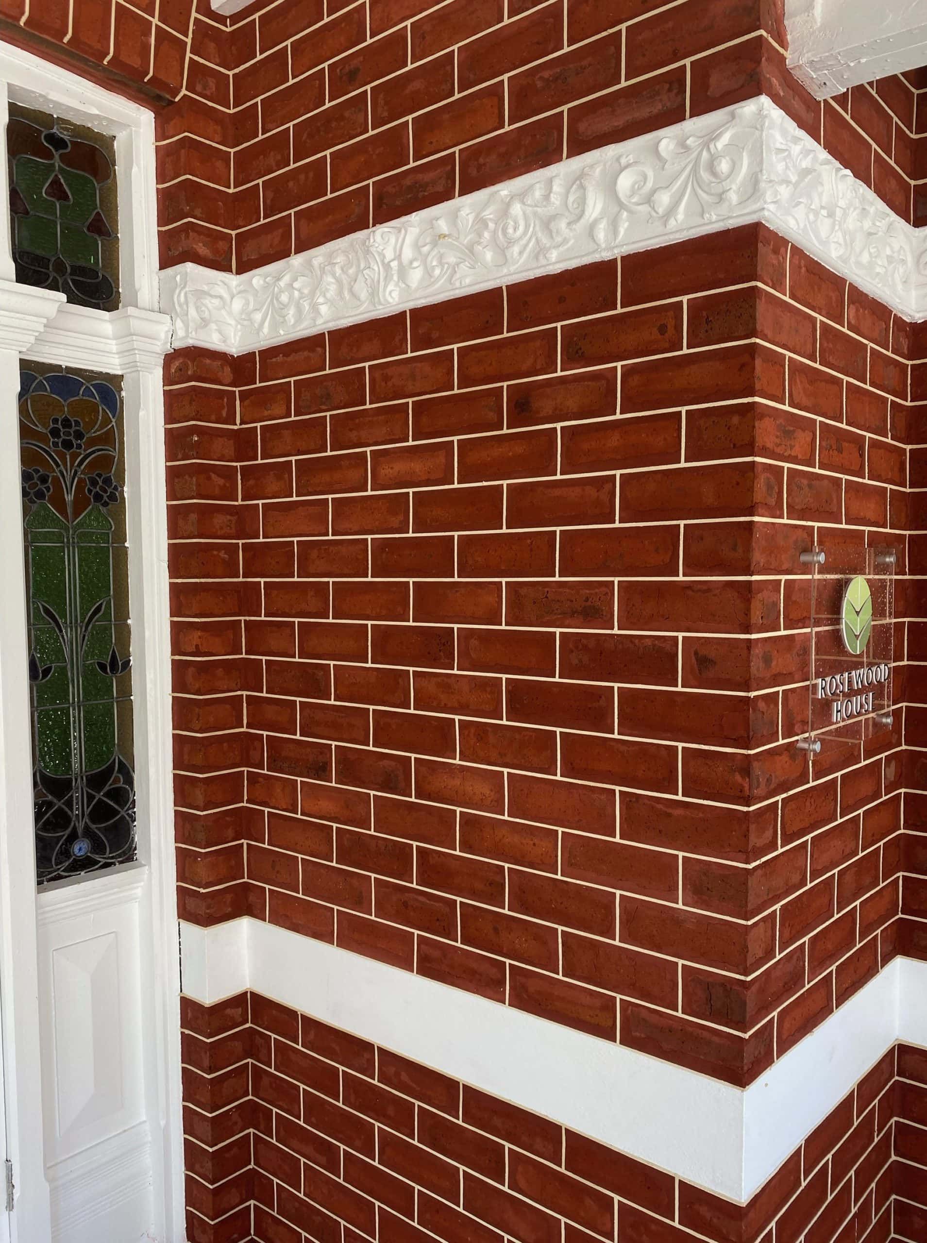 Red brick exterior wall with white trim and stained-glass door.