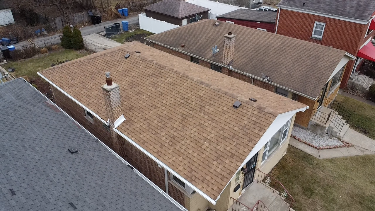 Gray asphalt shingle roof with white gutters on a light-colored building, outdoors with a blue sky.