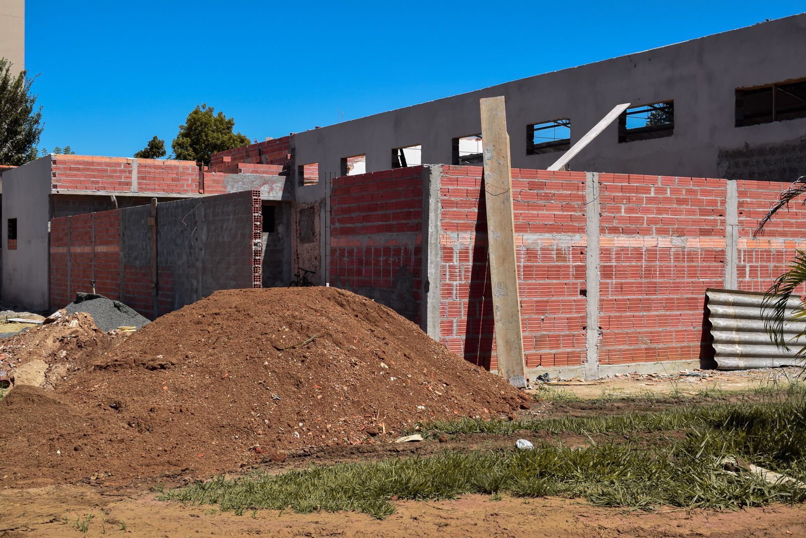 Construction site with red brick walls, dirt pile, and blue sky.