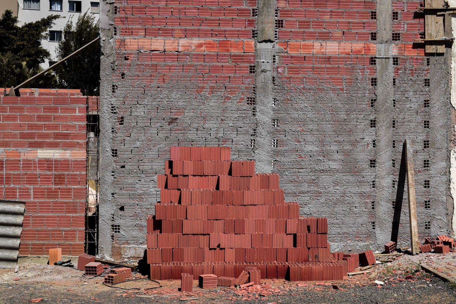 Construction site with red bricks stacked and a partially built brick wall. Concrete support beams visible.