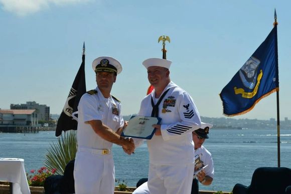 A man in a navy uniform shakes hands with another man