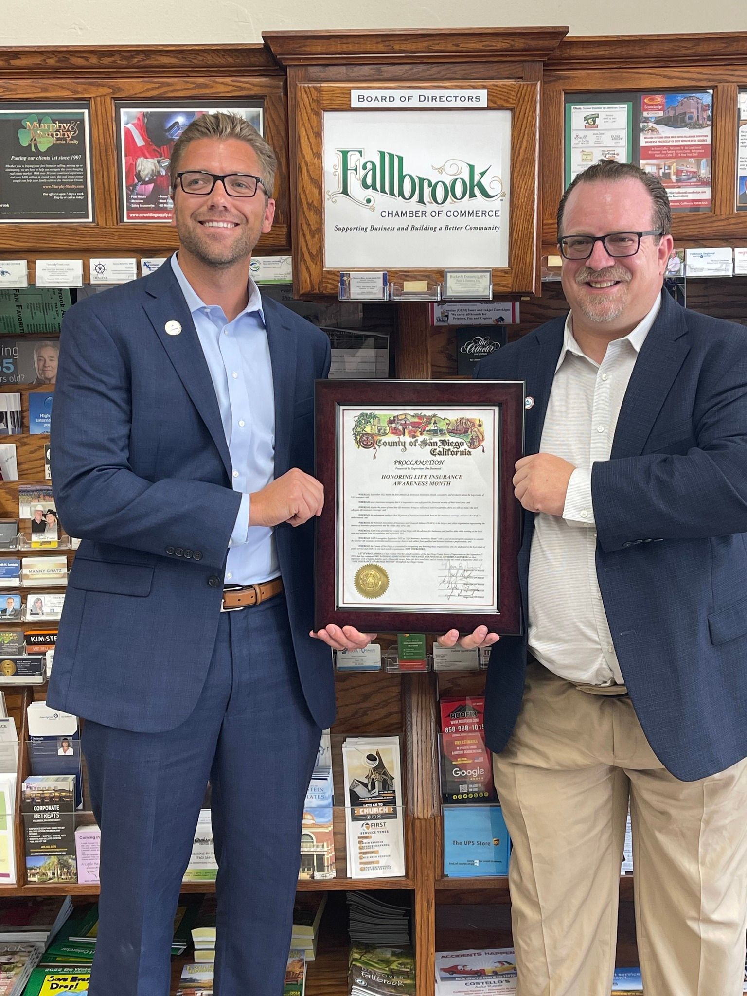 Two men holding a certificate in front of a sign that says fallbrook