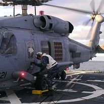 A man is working on a helicopter on a dock.