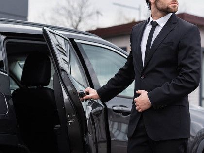 A man in a suit and tie is opening the door of a car.