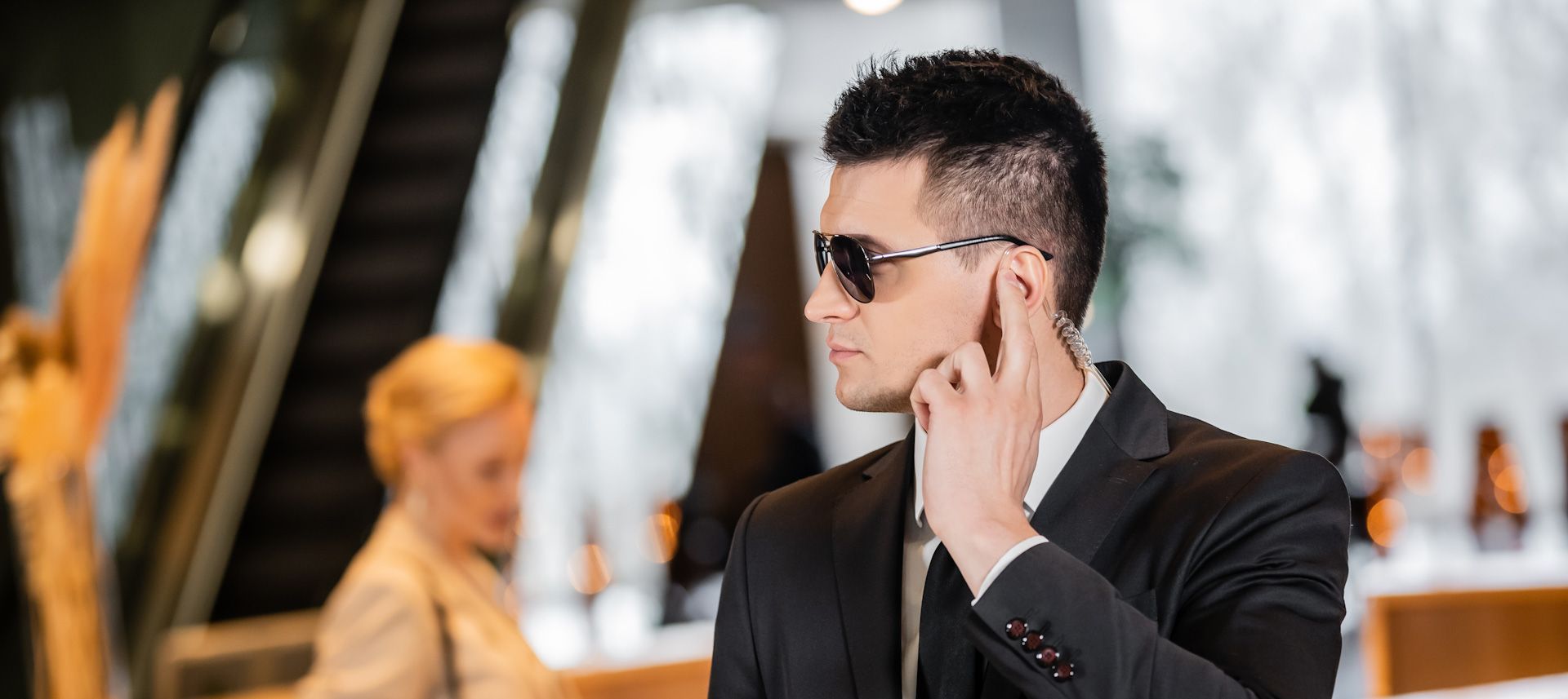 A man in a suit and sunglasses is talking on a cell phone.