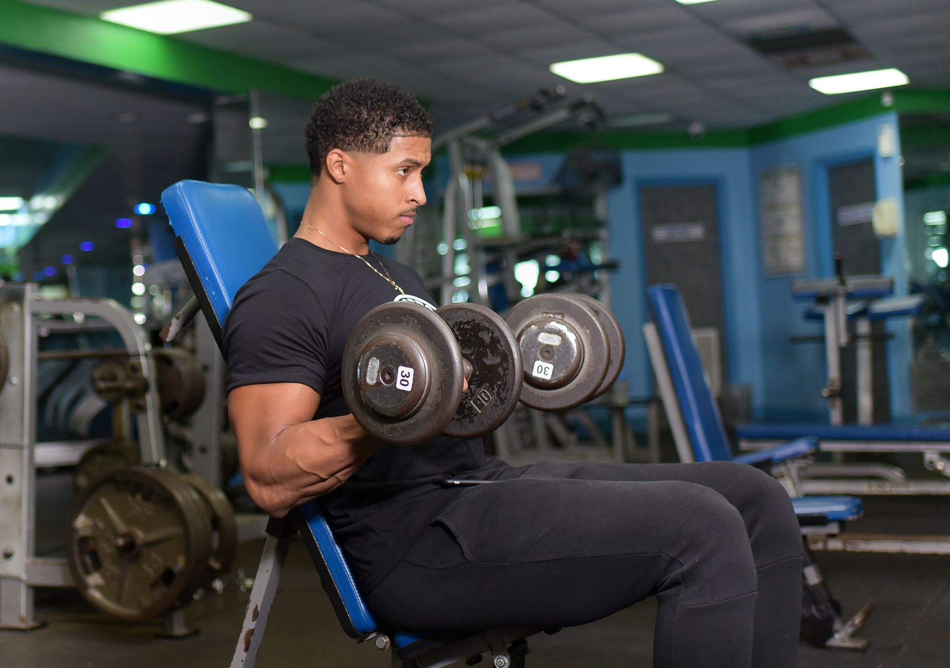 A man is sitting on a bench in a gym lifting dumbbells.