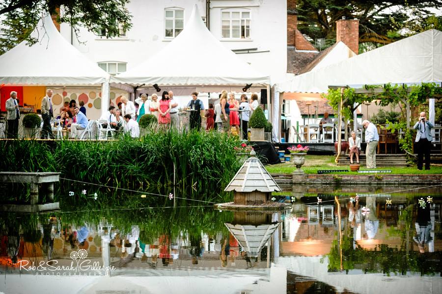 A group of people are standing in front of a building next to a pond.