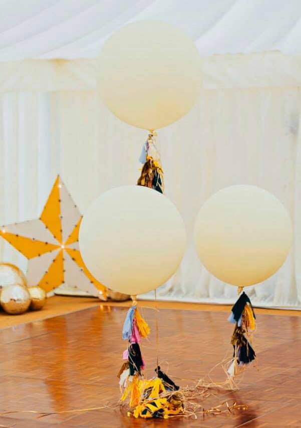 Three white balloons are hanging from a string on a wooden floor.