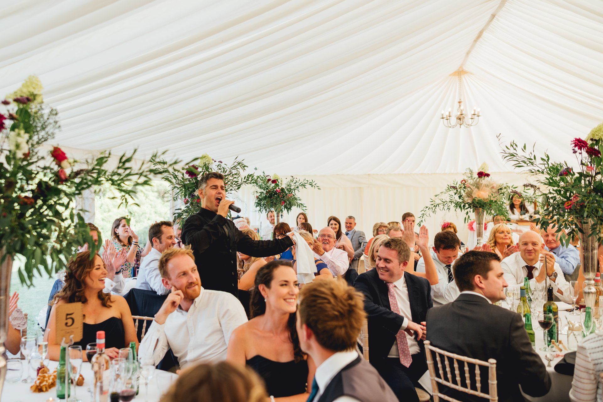 A man is standing in front of a crowd of people at a wedding reception.