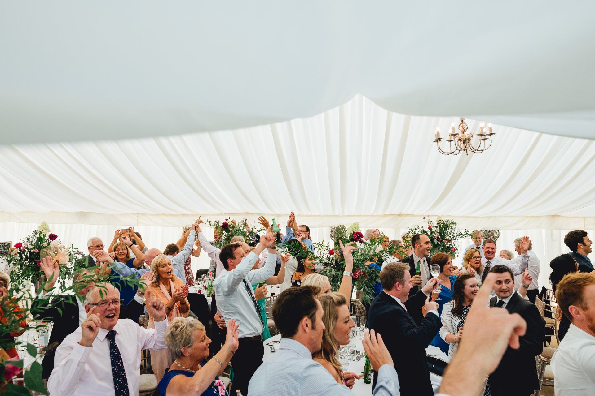 A large group of people are dancing in a tent at a wedding reception.
