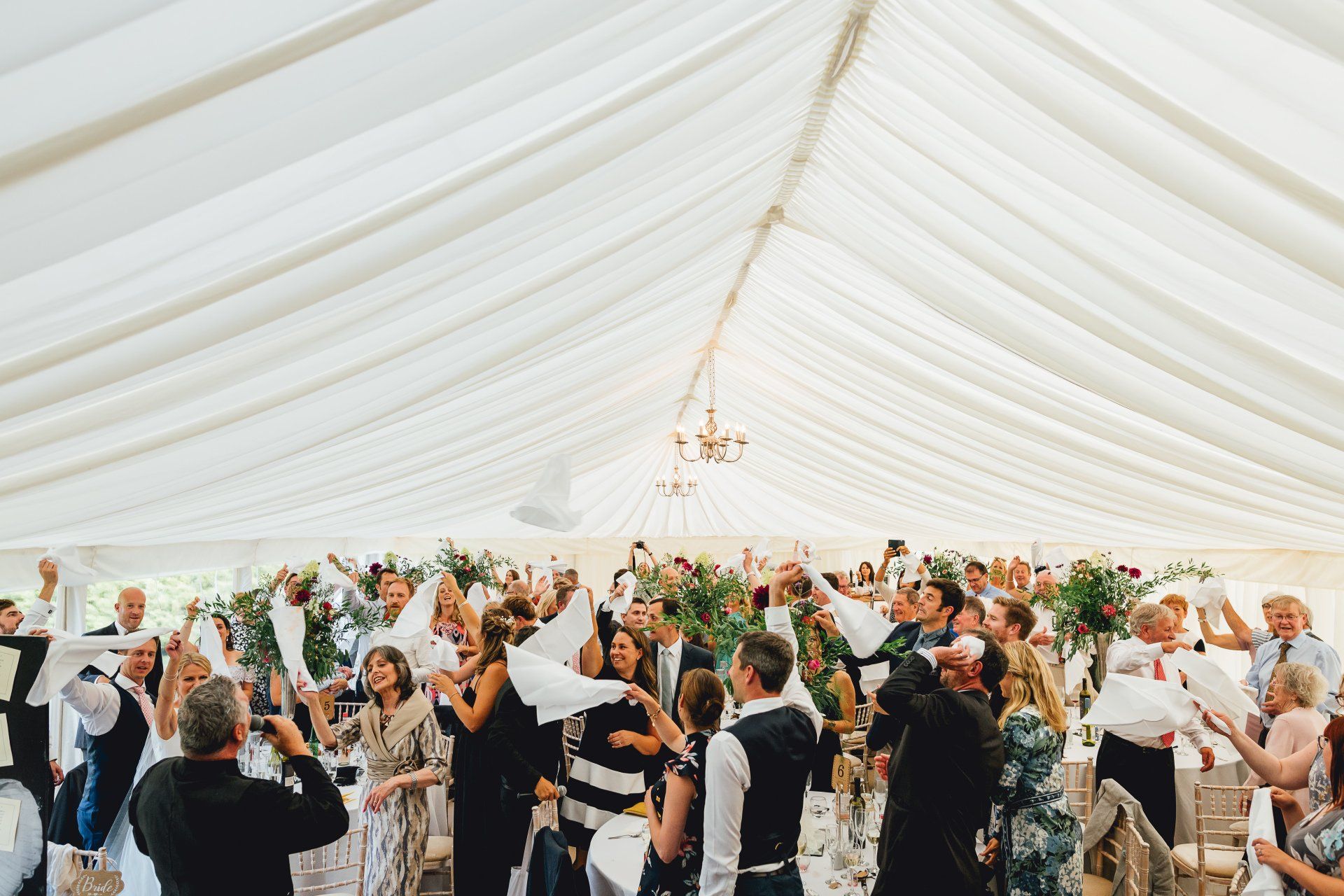 A large group of people are dancing in a tent at a wedding reception.