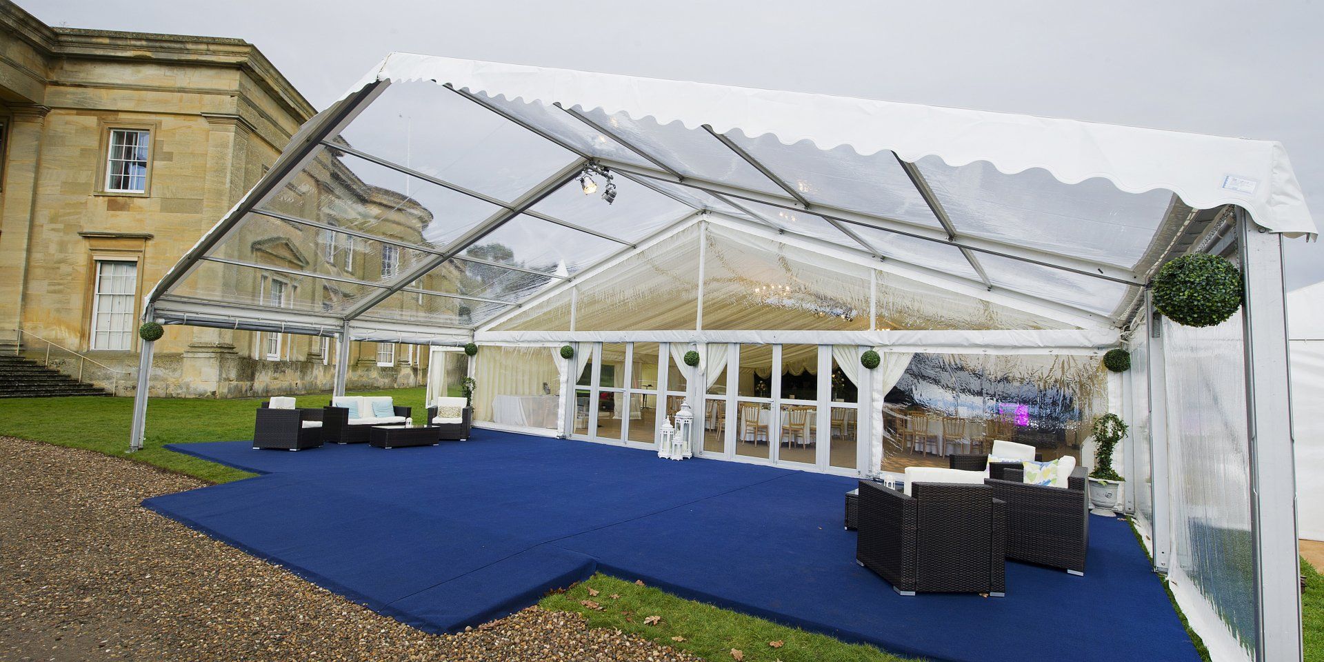 A clear tent is sitting on a blue carpet in front of a building.