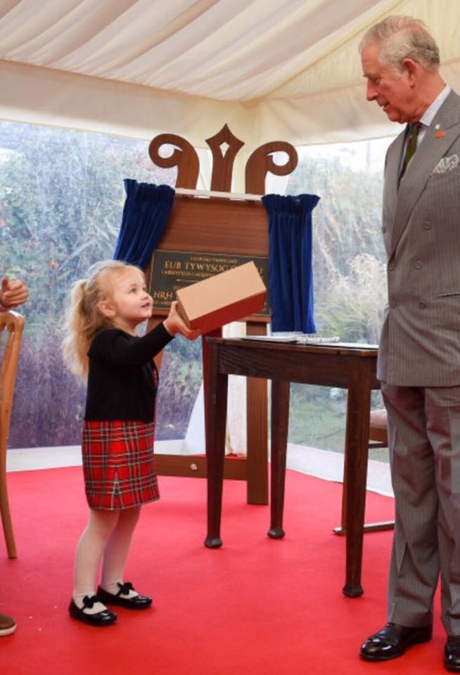 A little girl is holding a box in front of a man in a suit
