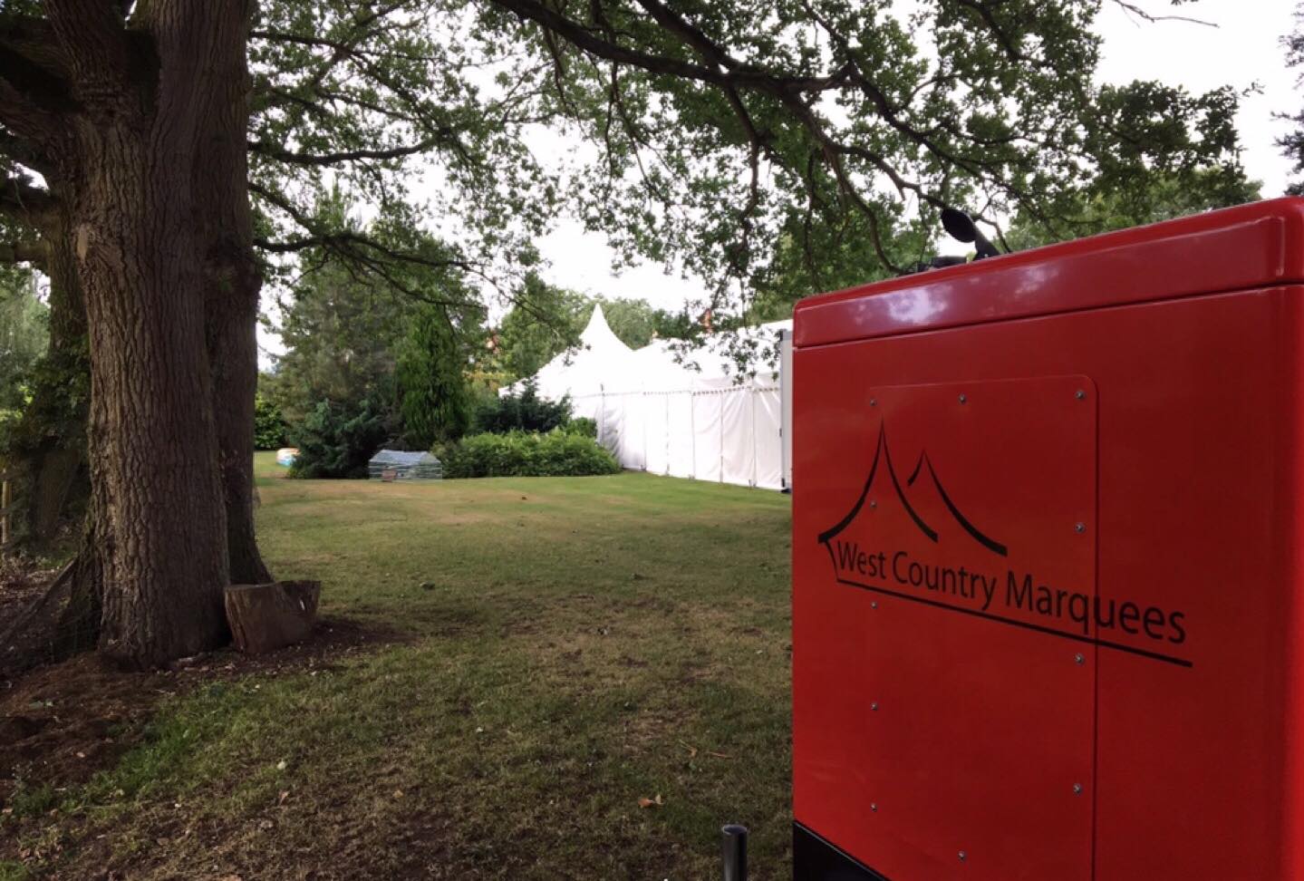 A red trailer is parked in a grassy field next to a tree.