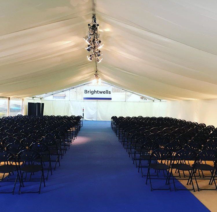 Rows of black folding chairs under a tent that says brightwells
