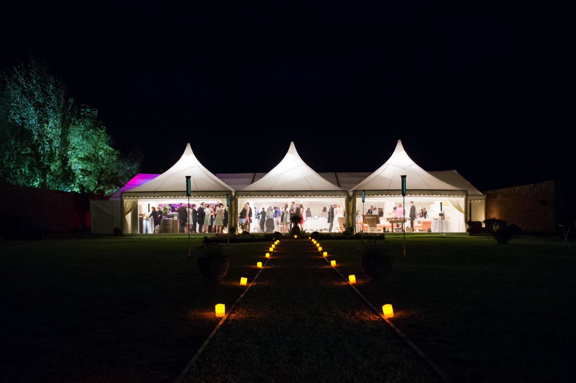A row of tents are lit up at night with candles in front of them.