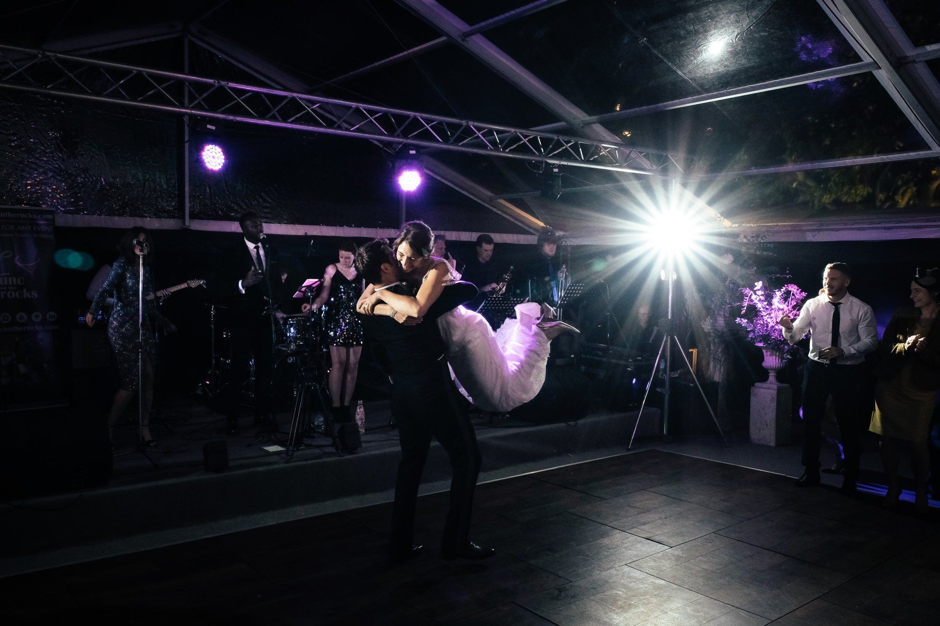 A man is holding a bride in his arms while they dance on a dance floor.