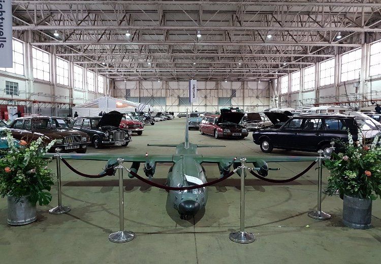 A large model airplane is on display in a hangar filled with cars