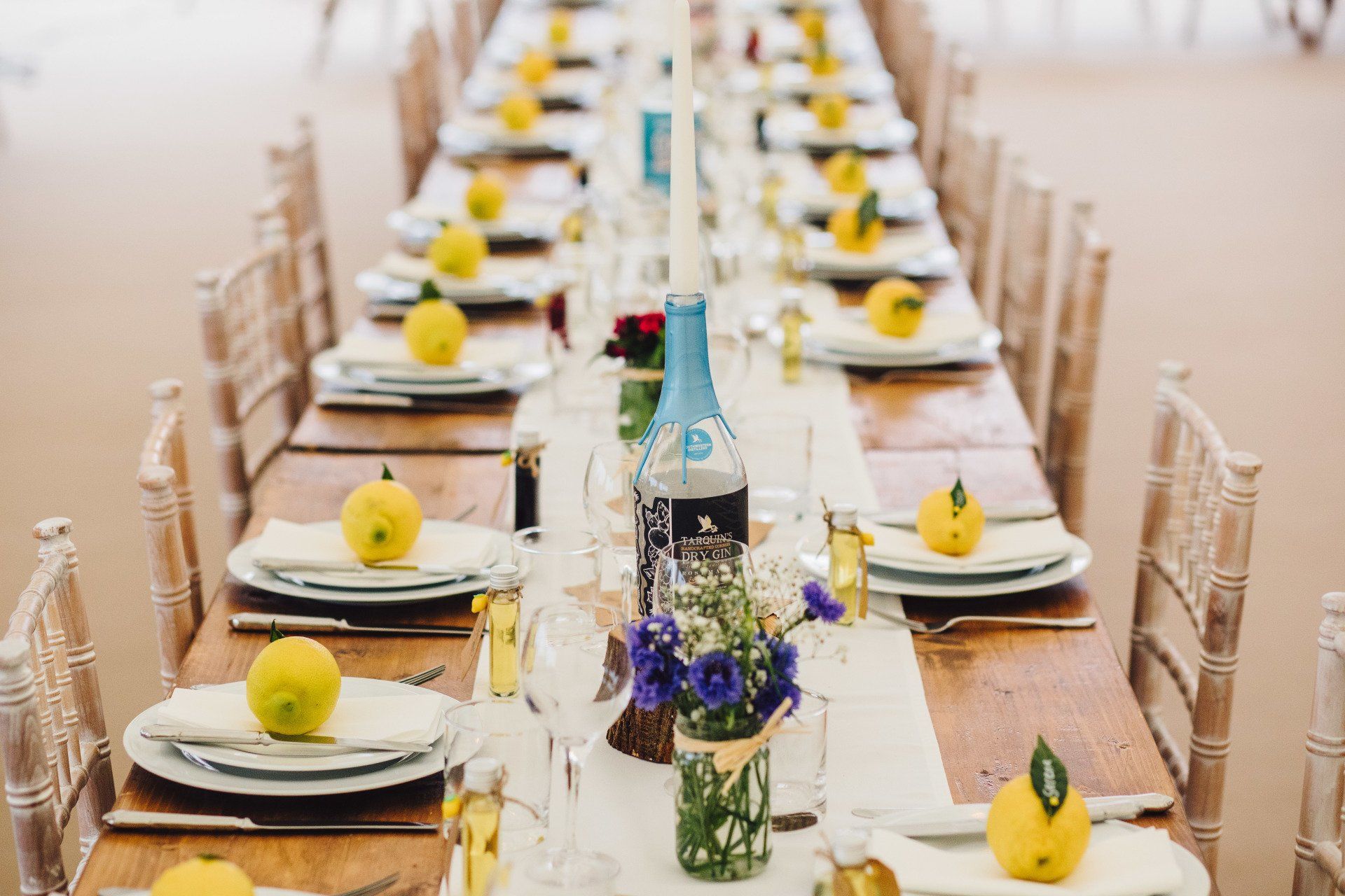 A long table with plates , glasses , and lemons on it.