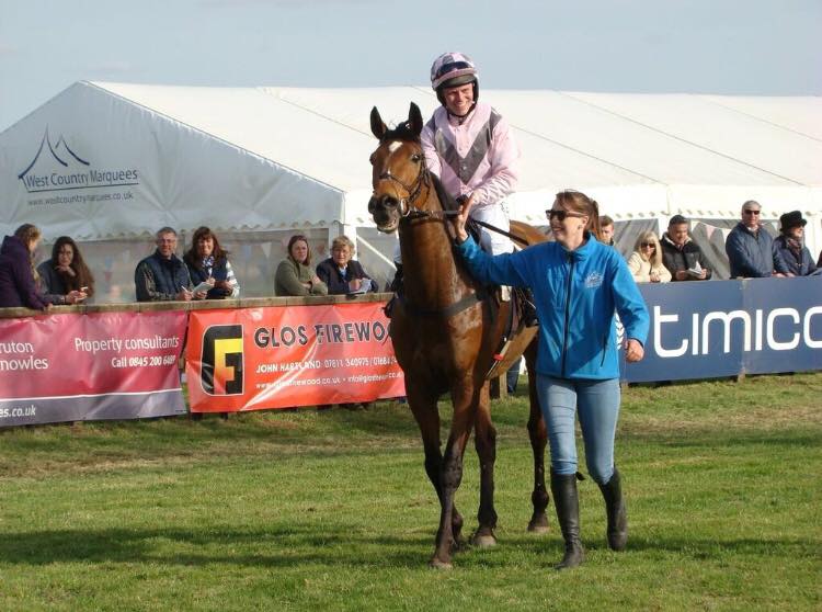 A woman leading a horse in front of a sign that says timco