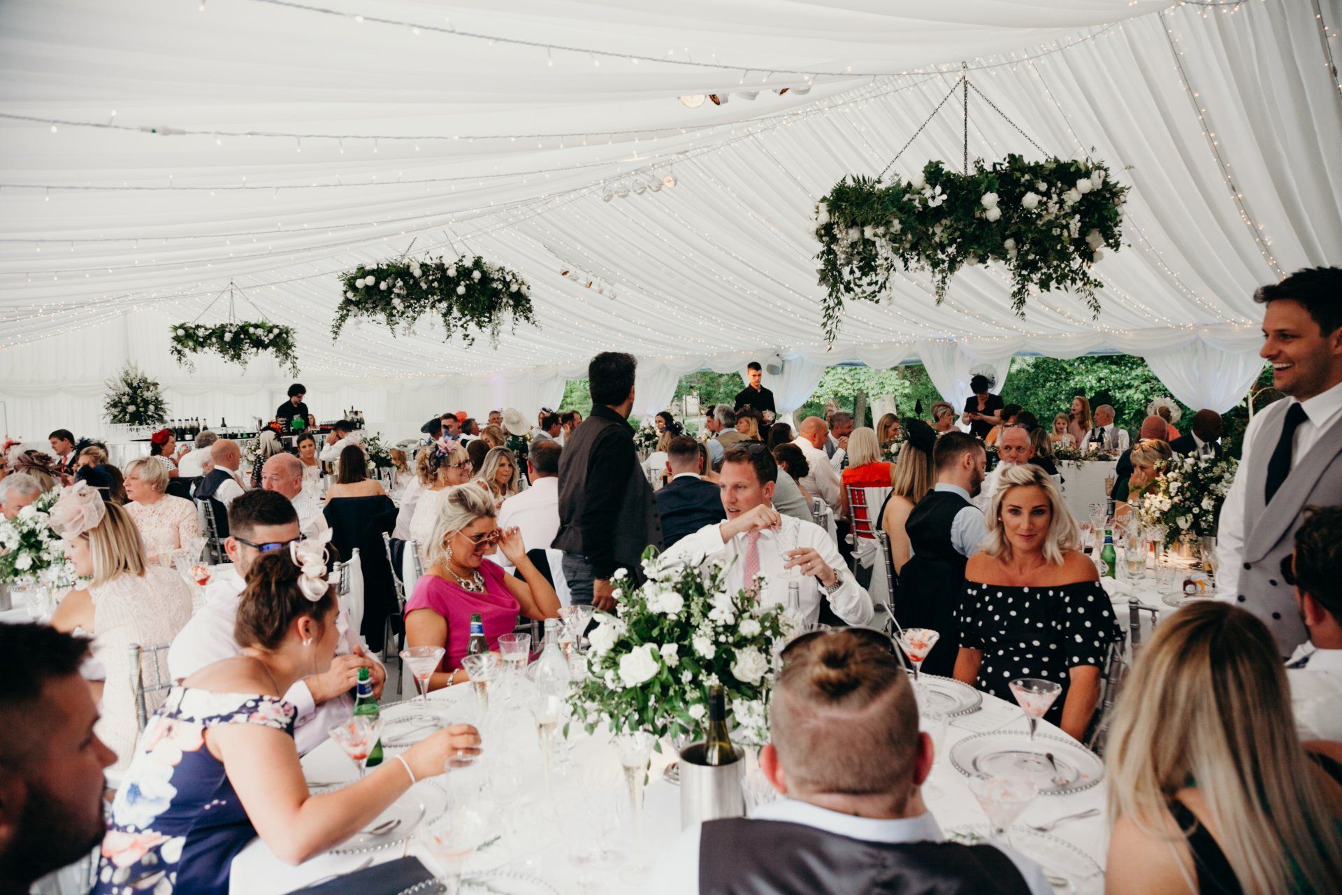 A large group of people are sitting at tables in a tent at a wedding reception.