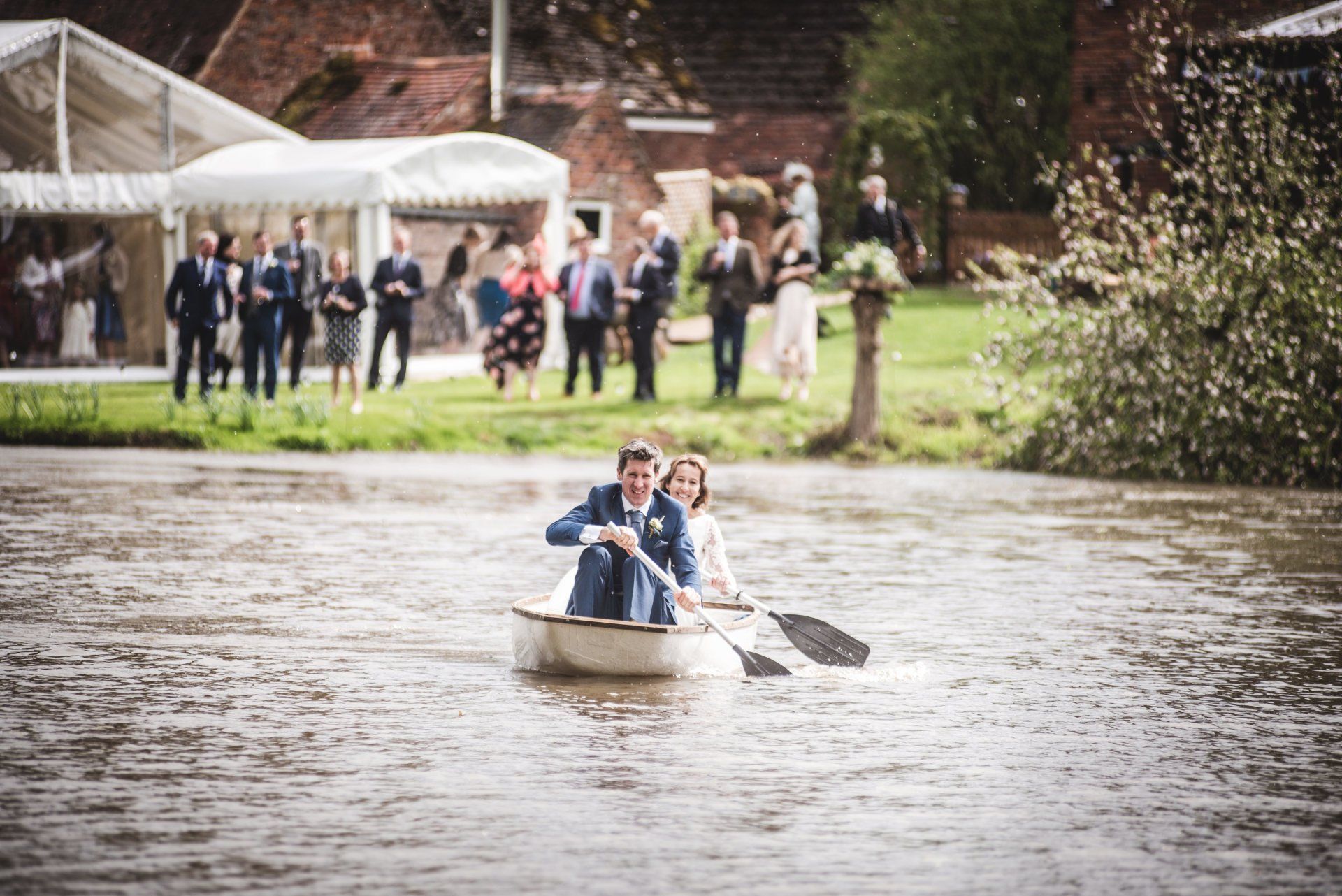 A bride and groom are rowing a boat on a river.