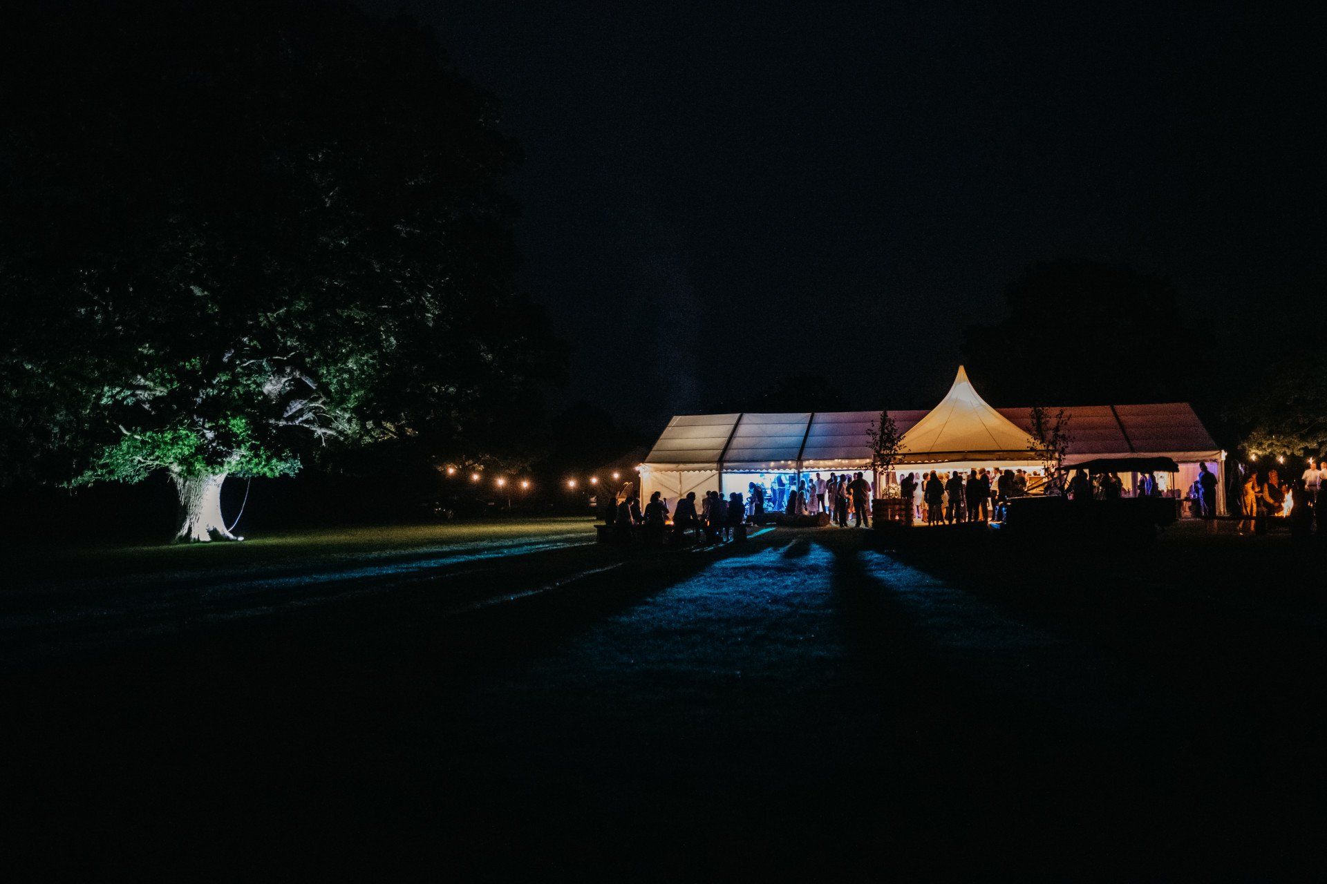 A group of people are standing in front of a tent at night.