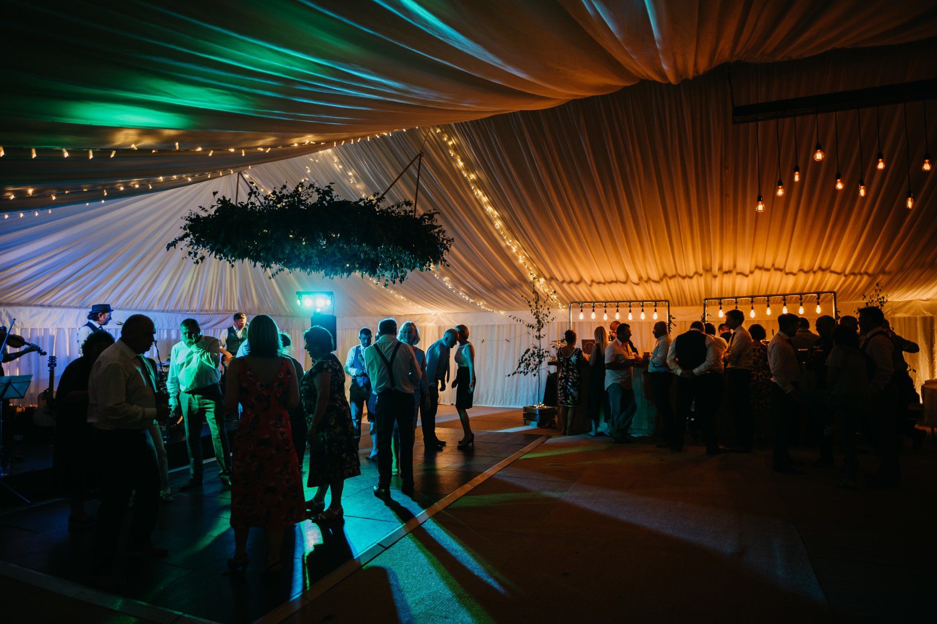 A group of people are dancing in a tent at a wedding reception.