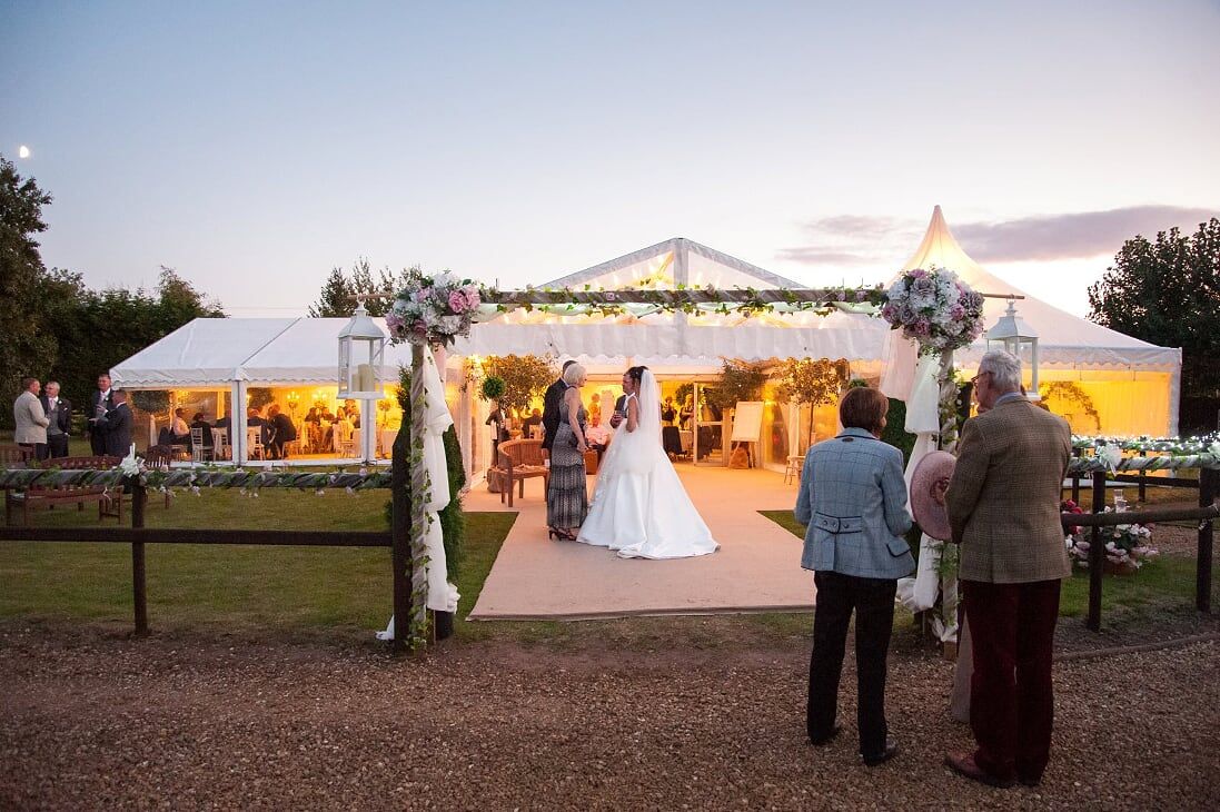 A bride and groom are standing in front of a tent at a wedding reception.