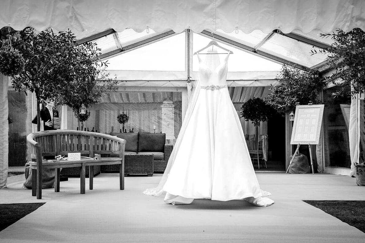 A black and white photo of a wedding dress hanging in a tent.