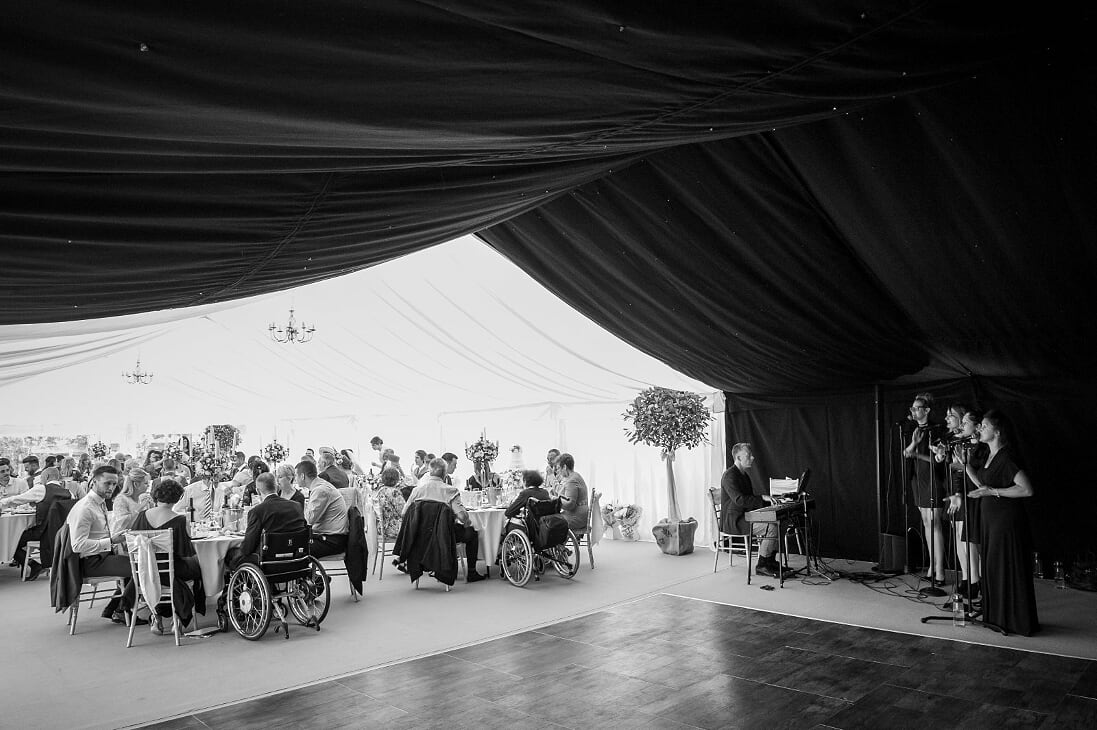 A group of people in wheelchairs are sitting at tables in a tent.