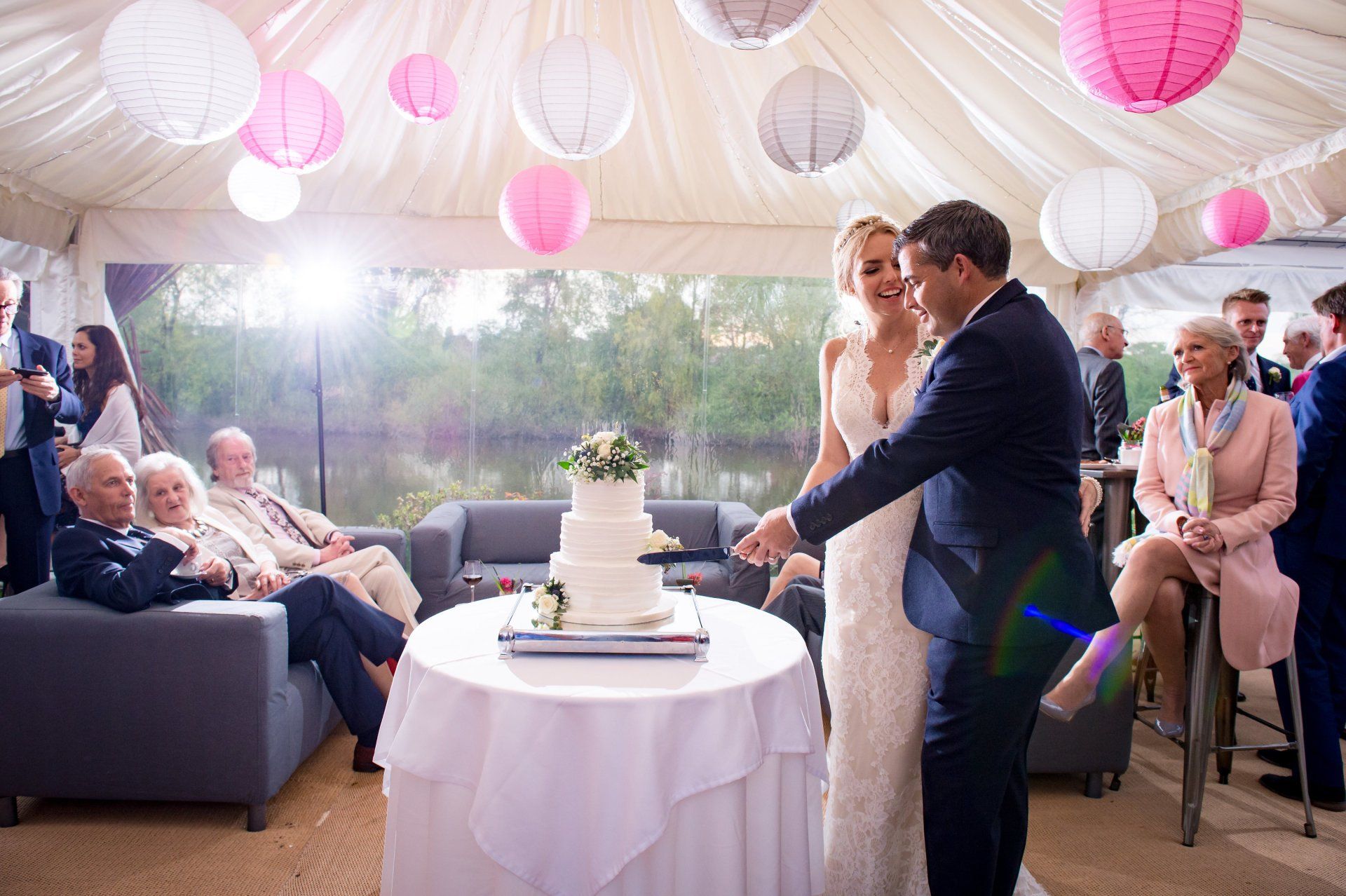 A bride and groom are cutting their wedding cake in a tent.