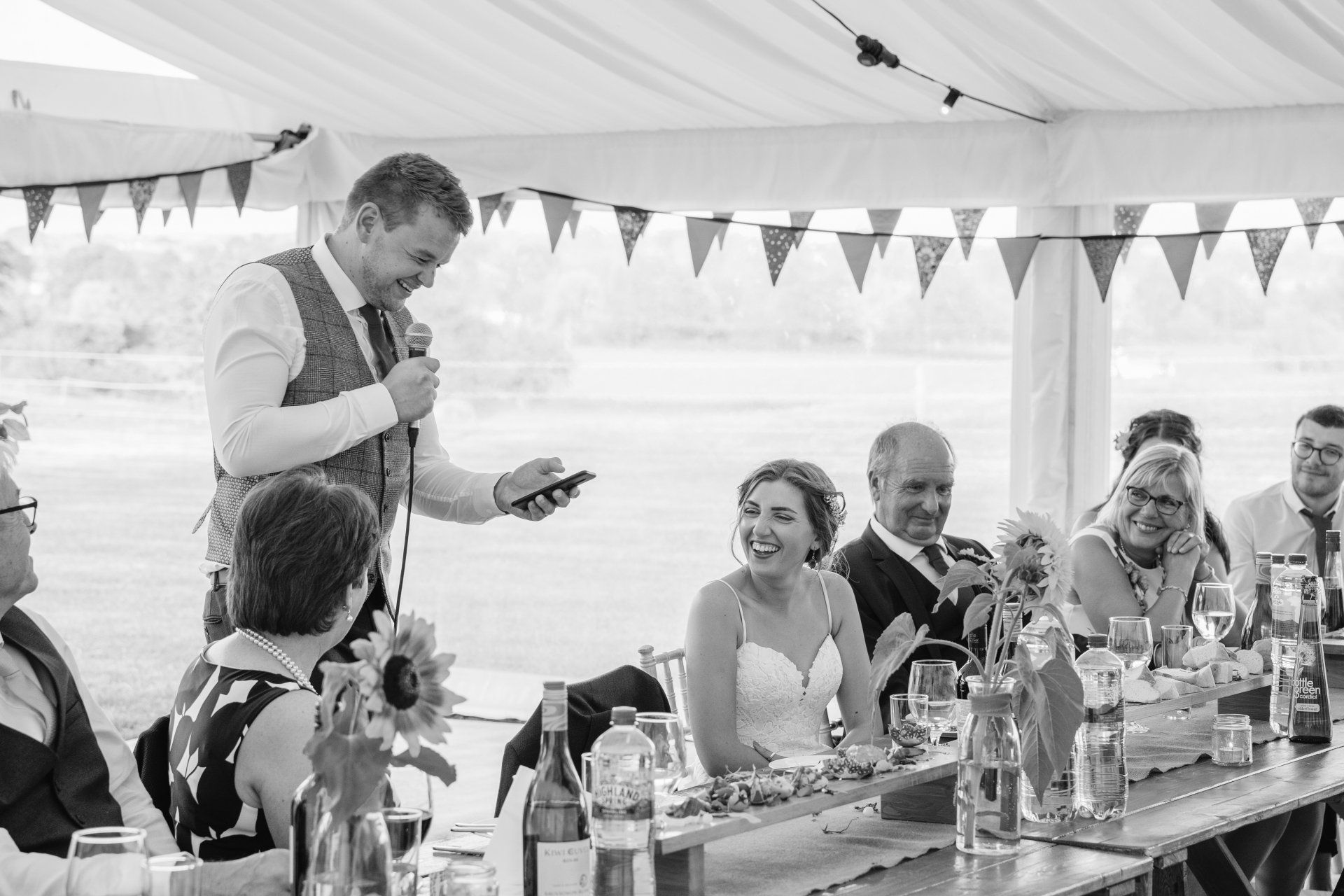 A man is giving a speech at a wedding reception in a tent.