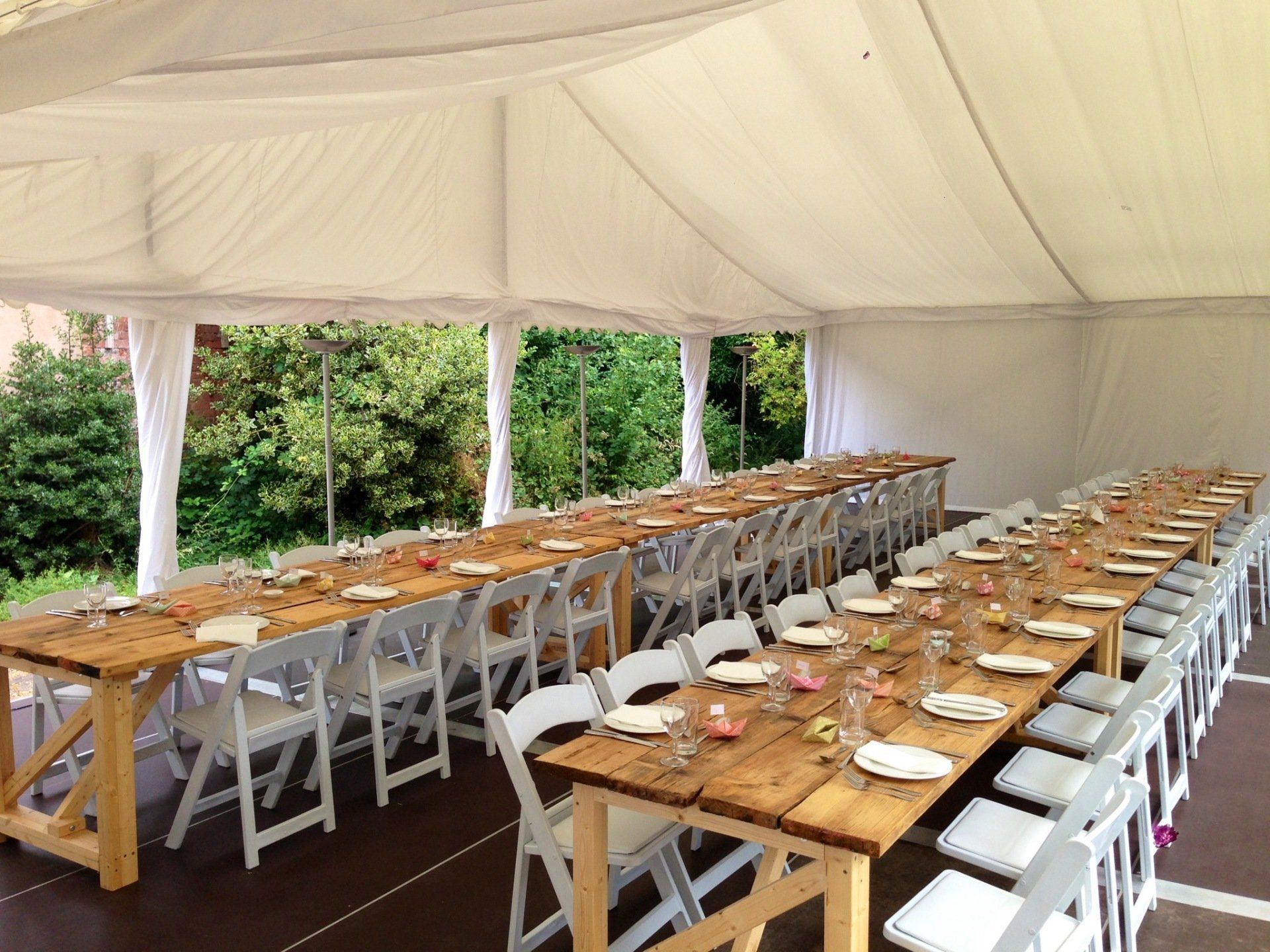 A long wooden table with white chairs under a tent.