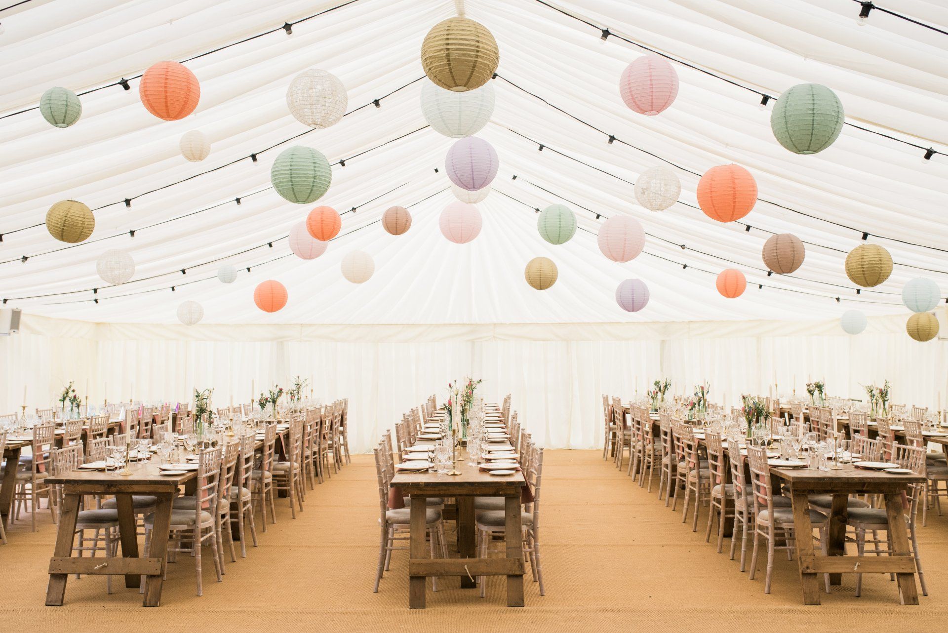 A large tent with tables and chairs and paper lanterns hanging from the ceiling.