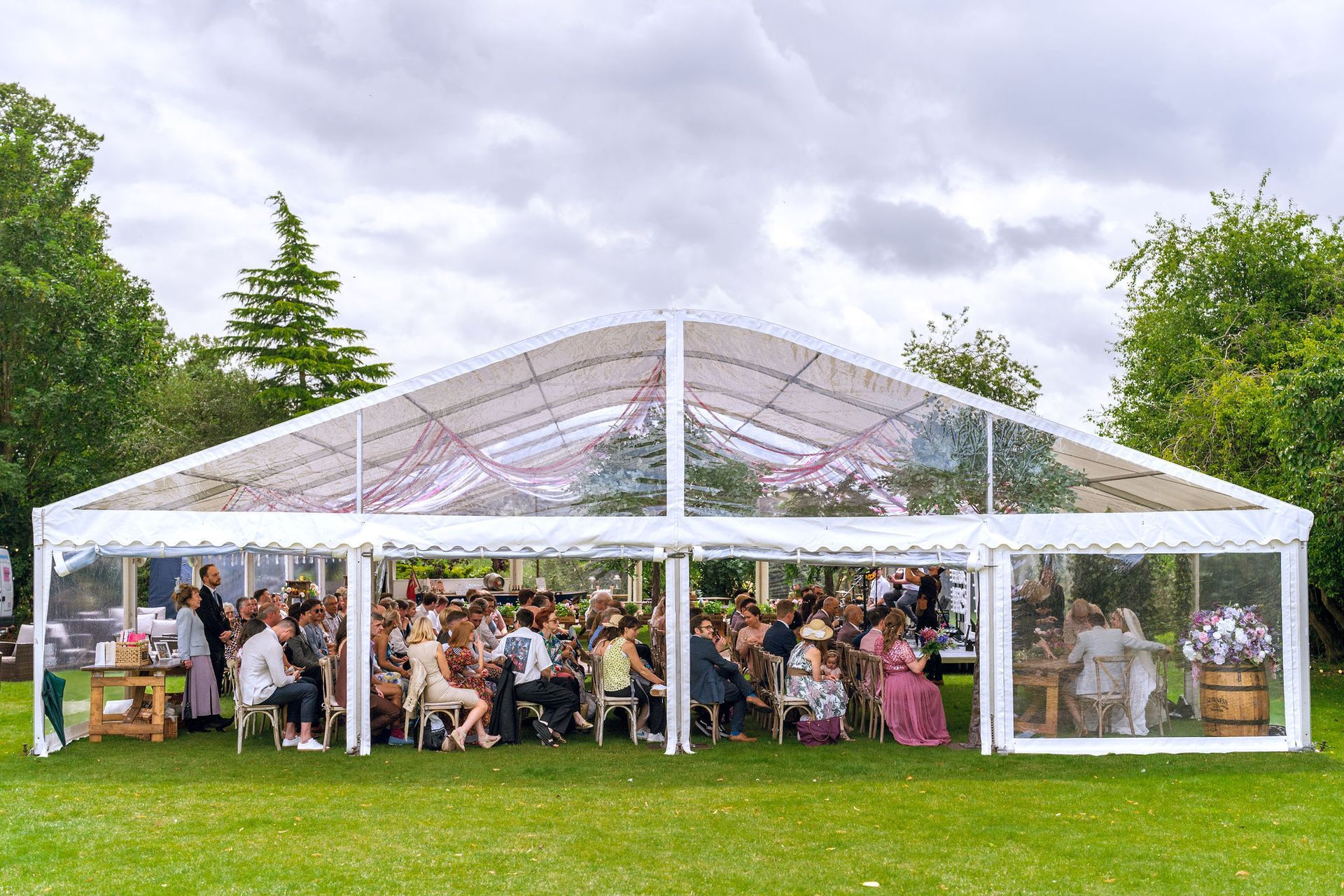 A group of people are sitting under a clear tent in a field.