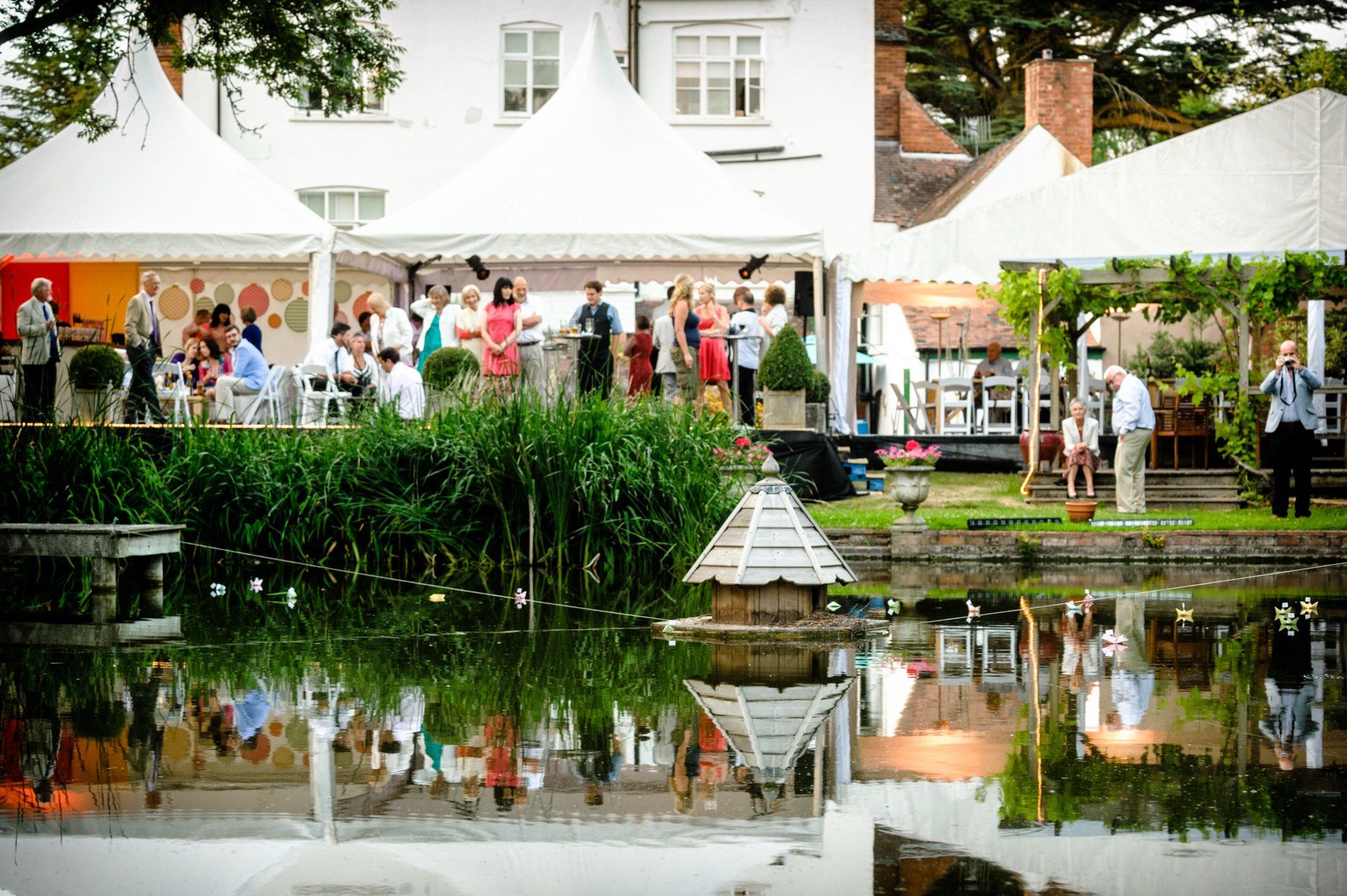 A group of people are standing in front of a white tent near a body of water.