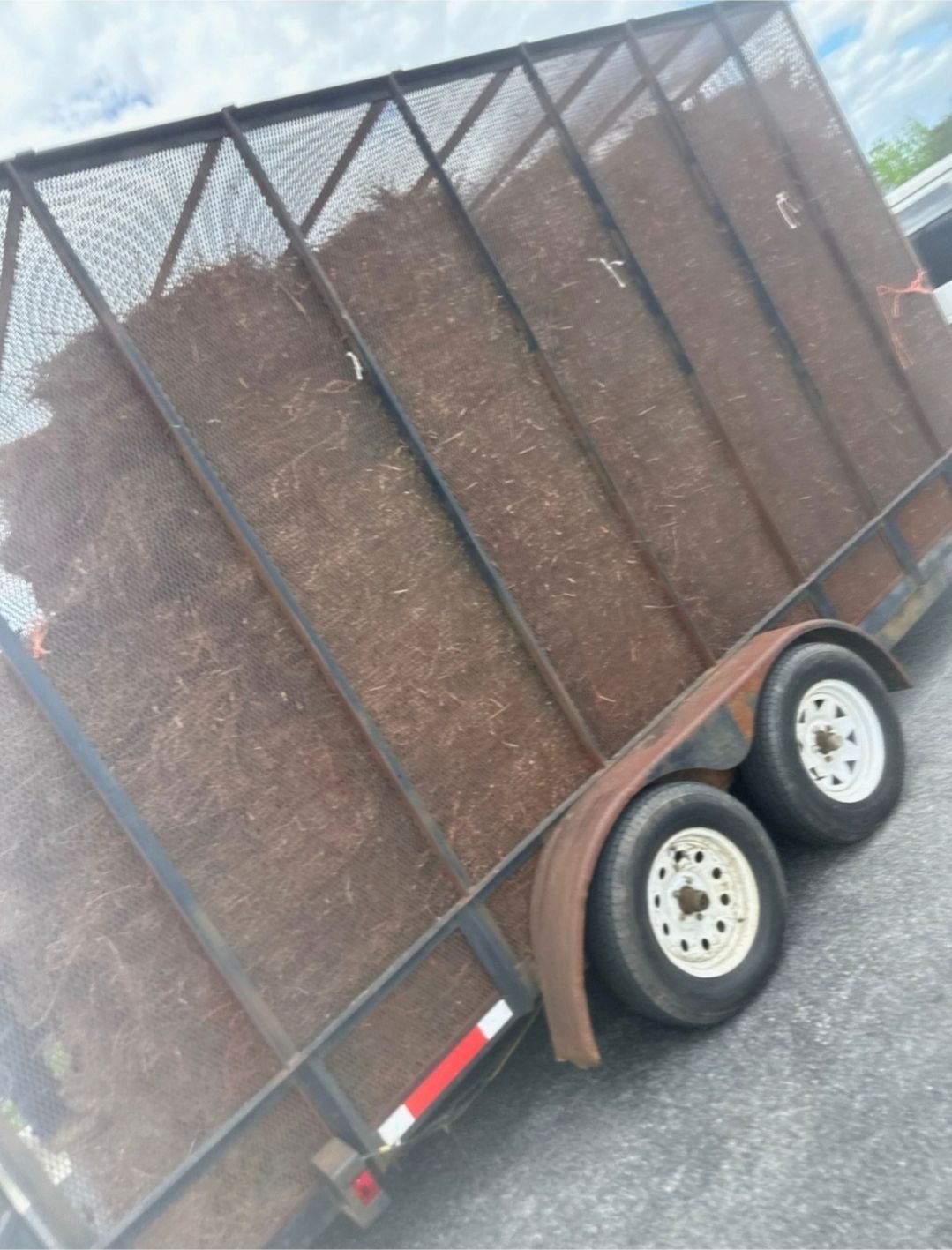 A trailer filled with hay is parked on the side of the road.