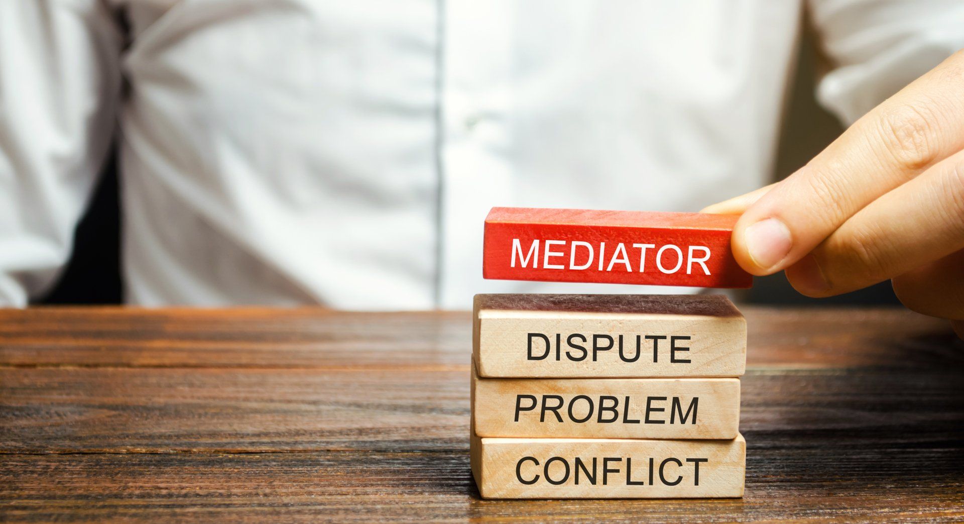 a person is stacking wooden blocks that say mediator dispute problem conflict