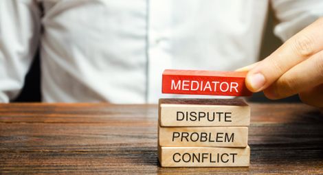 a person is stacking wooden blocks that say mediator dispute problem conflict