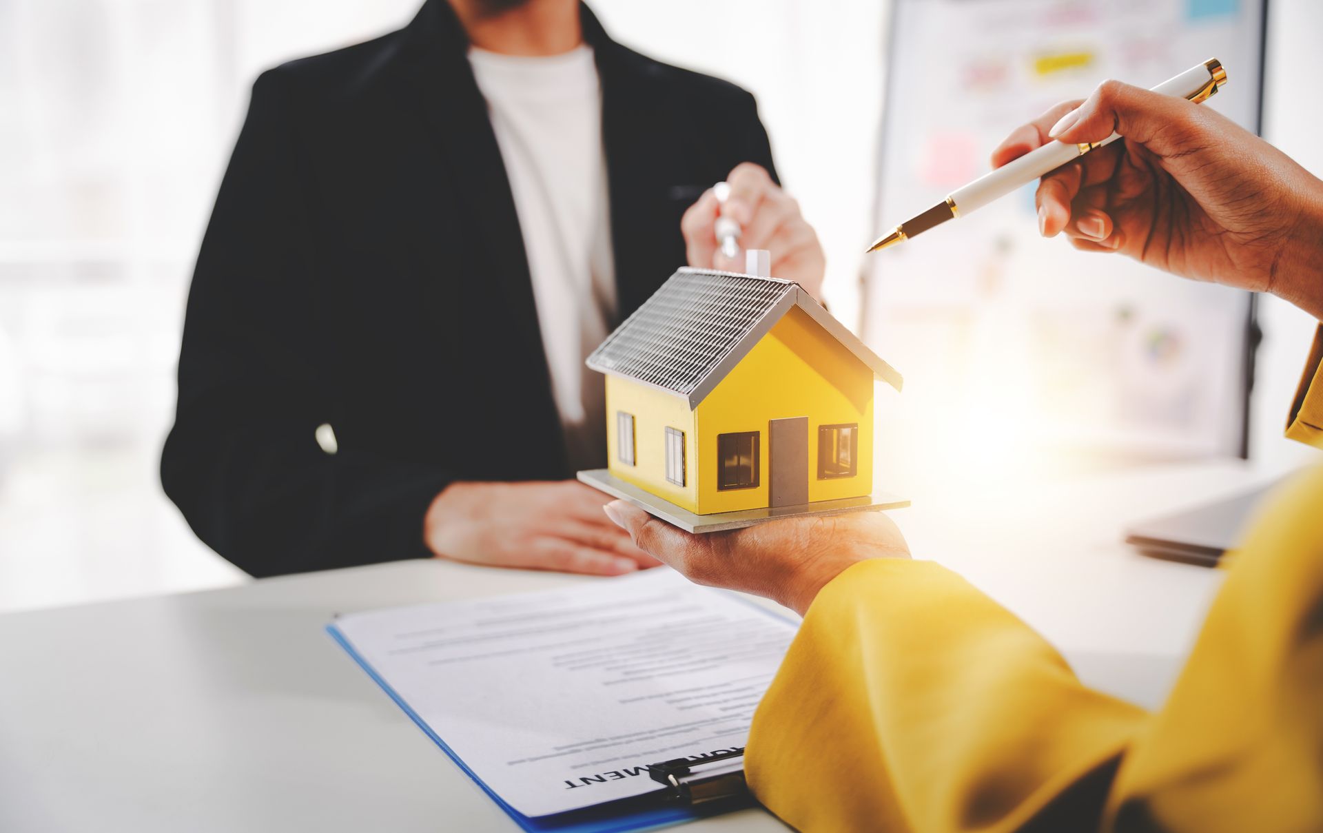 A person is holding a model house in front of a woman.