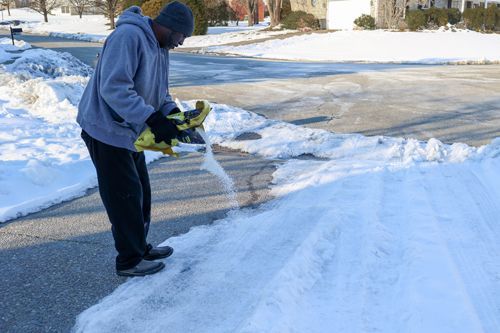 Person spreads salt on snowy driveway to prevent icy buildup.