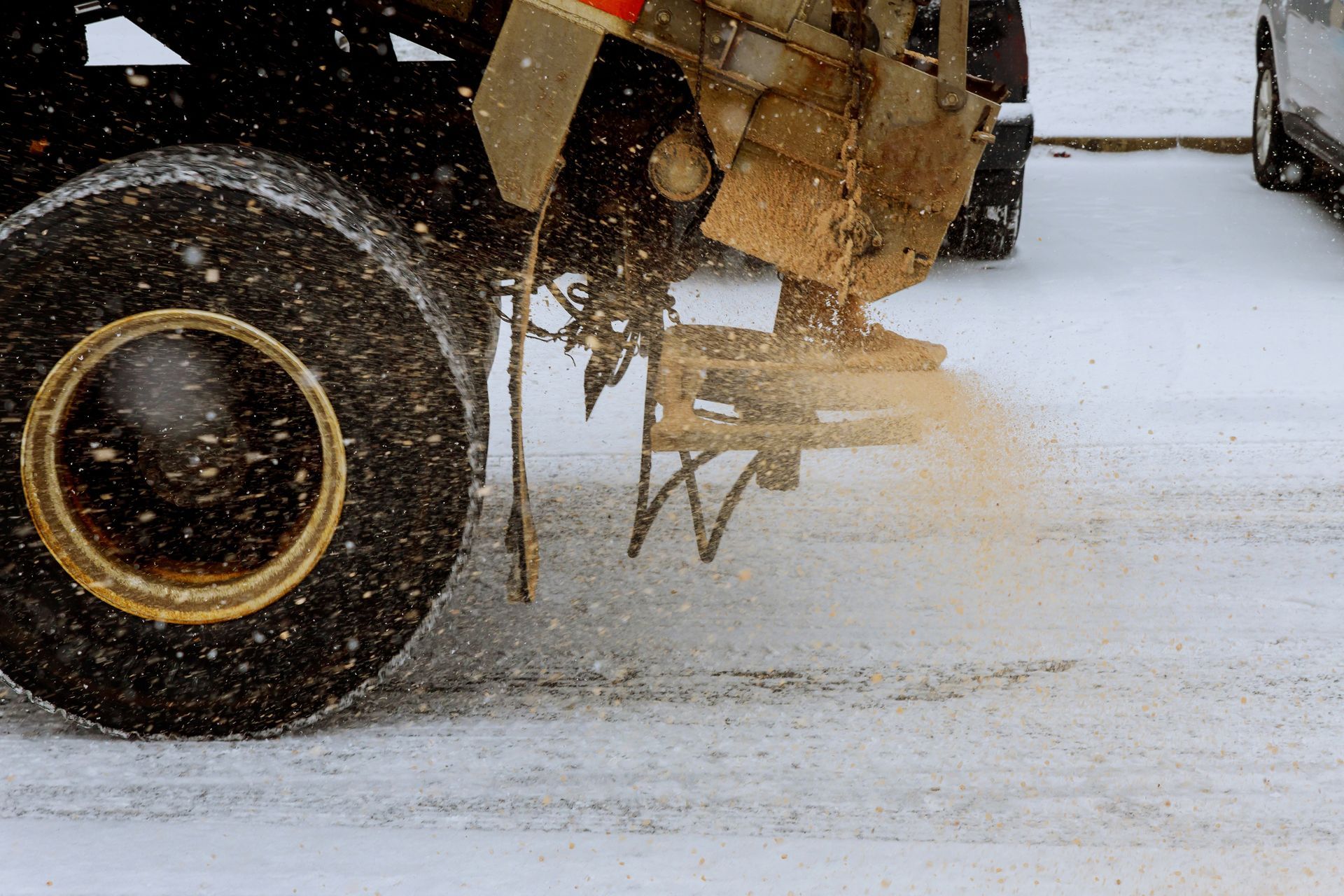 Salt truck spreading material on a snowy road, close-up of a tire and spreader.