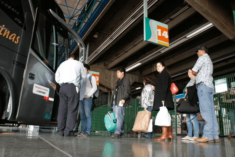 Homem na sala de controle falando ao telefone, supervisionando ônibus estacionados ao ar livre sob abrigo.