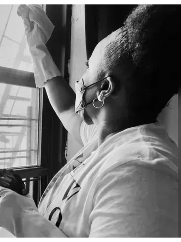 Person cleaning a window, wearing gloves, in black and white.