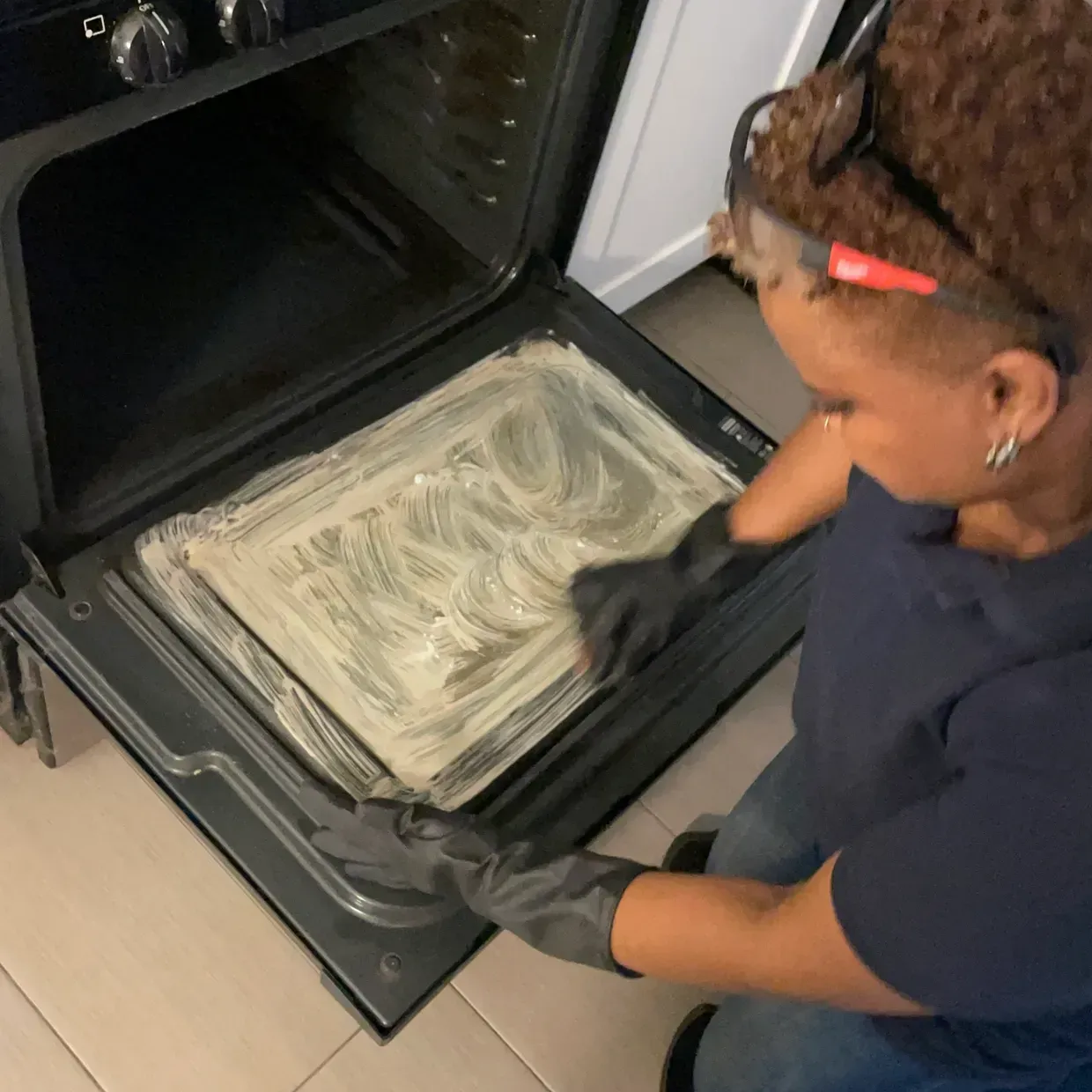 Person cleaning an oven interior with cleaning product and gloves.