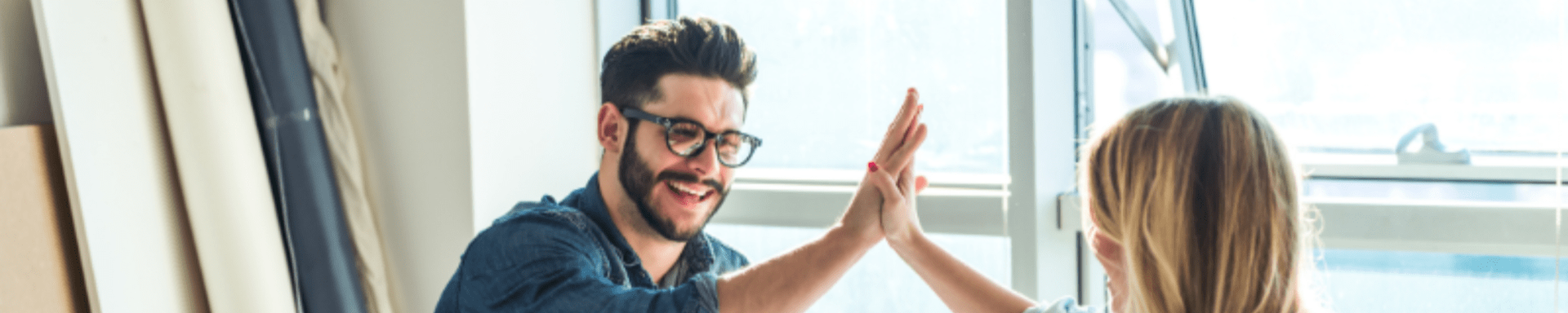 A man and a woman are giving each other a high five in front of a window.